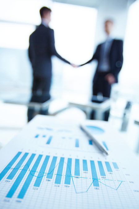 Financial chart Business document and pen on desk with two employees handshaking on background